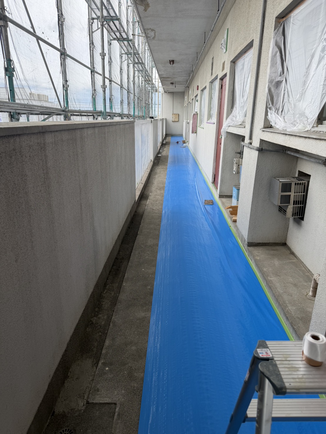 アパート共用廊下の窓まわりを養生して外壁塗装を進めている様子